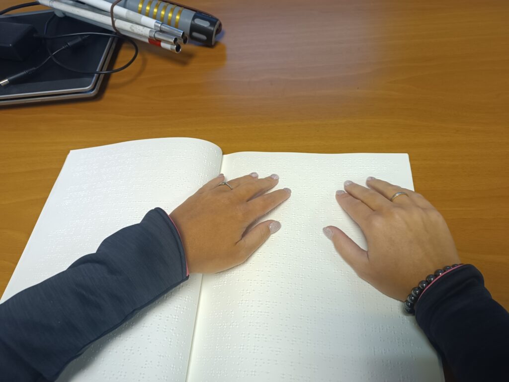 Asztalon kinyitva a Braille írásos Hírmondó, az olvasó kezei is látszanak