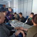 Egy asztal körül ülnek a tagok és az egyik munkatárs a virágmag ültetés menetéről beszél