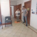 A folyosón kialakított tekepályán egy résztvevő éppen dobni készül a tekegolyót helyettesítő labdával, mellette egy segítő is látszik