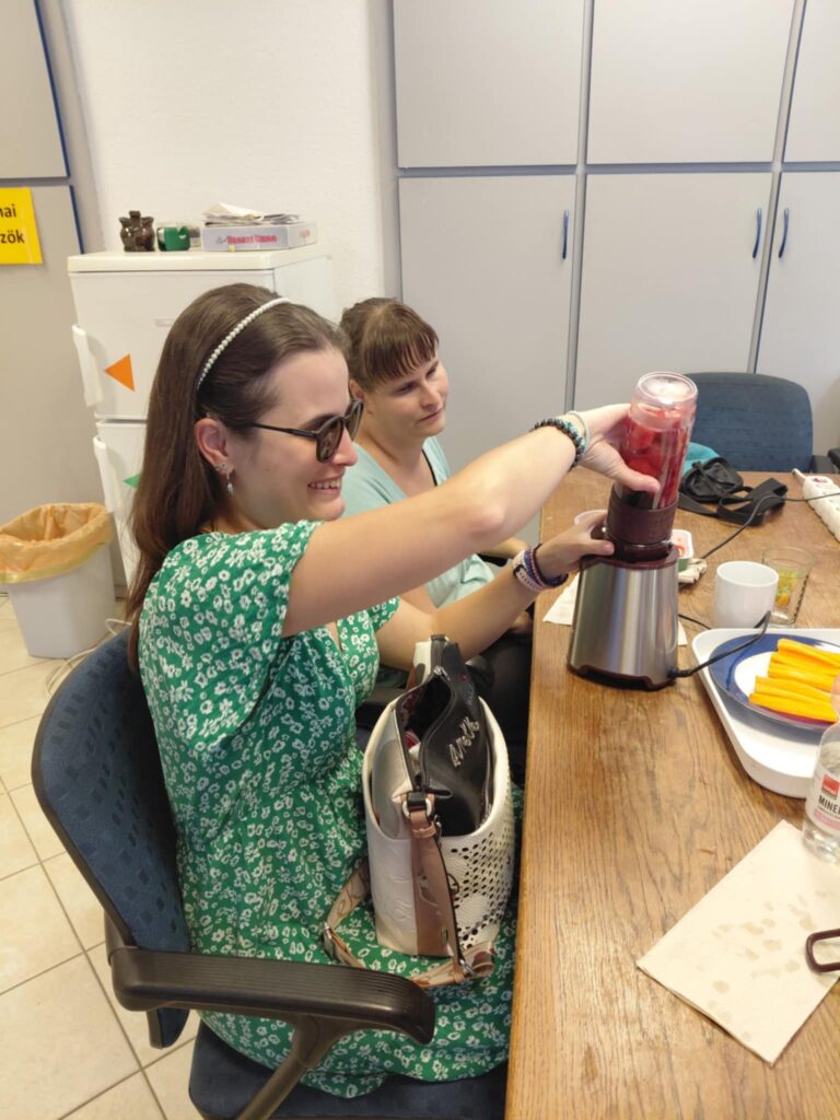 Elsőként próbálja ki a Smoothie készítő gépet a klub főszervezője, profin illeszti a turmixgépre az üveget, mellette egy másik résztvevő ül