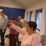 A résztvevők állnak és különböző tornagyakorlatokat végeznek, hogy bemelegítsenek az énekléshez