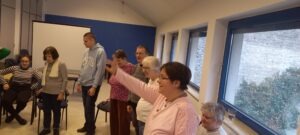 A résztvevők állnak és különböző tornagyakorlatokat végeznek, hogy bemelegítsenek az énekléshez