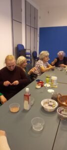 Györgyi, a foglalkozás vezetője és mellette 3 résztvevő elmélyülten fűzik a gyöngyöt