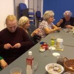 Györgyi, a foglalkozás vezetője és mellette 3 résztvevő elmélyülten fűzik a gyöngyöt