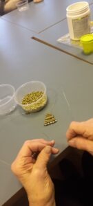 Két kéz, ahogy éppen valaki fűzi a gyöngyöt, a gyöngyangyal teste van kész