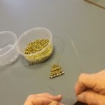 Két kéz, ahogy éppen valaki fűzi a gyöngyöt, a gyöngyangyal teste van kész