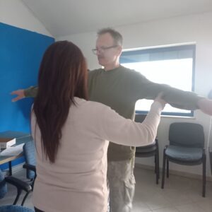 Egyik siketvak tagunk látható szintén oldalra nyújtott karokkal vele szemben állva a jeltolmács segít neki