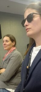Kőrösiné Dr. Babinszki Vera, mellette személyi segítője ülnek és hallgatják az előadást 