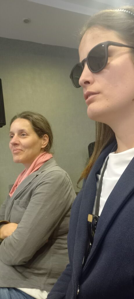 Kőrösiné Dr. Babinszki Vera, mellette személyi segítője ülnek és figyelnek a közlekedési konferencián
