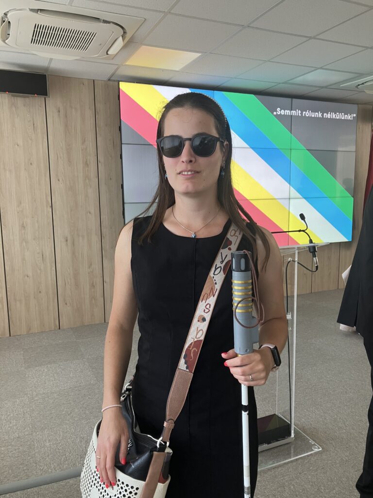 Kőrősiné Dr. Babinszki Vera áll egy tábla előtt, aminek a jobb felső sarkában ez szerepel, Semmit rólunk nélkülünk