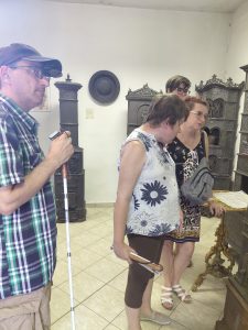 Két tagunk és egy kísérő látszik, ahogy a bemutatóteremben hallgatják az előadást