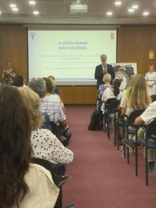 Dr. Kaló Zoltán főigazgató egy kivetített diakép előtt, amin az a felirat olvasható, A KÖZÖS MUNKA MOST KEZDŐDIK!